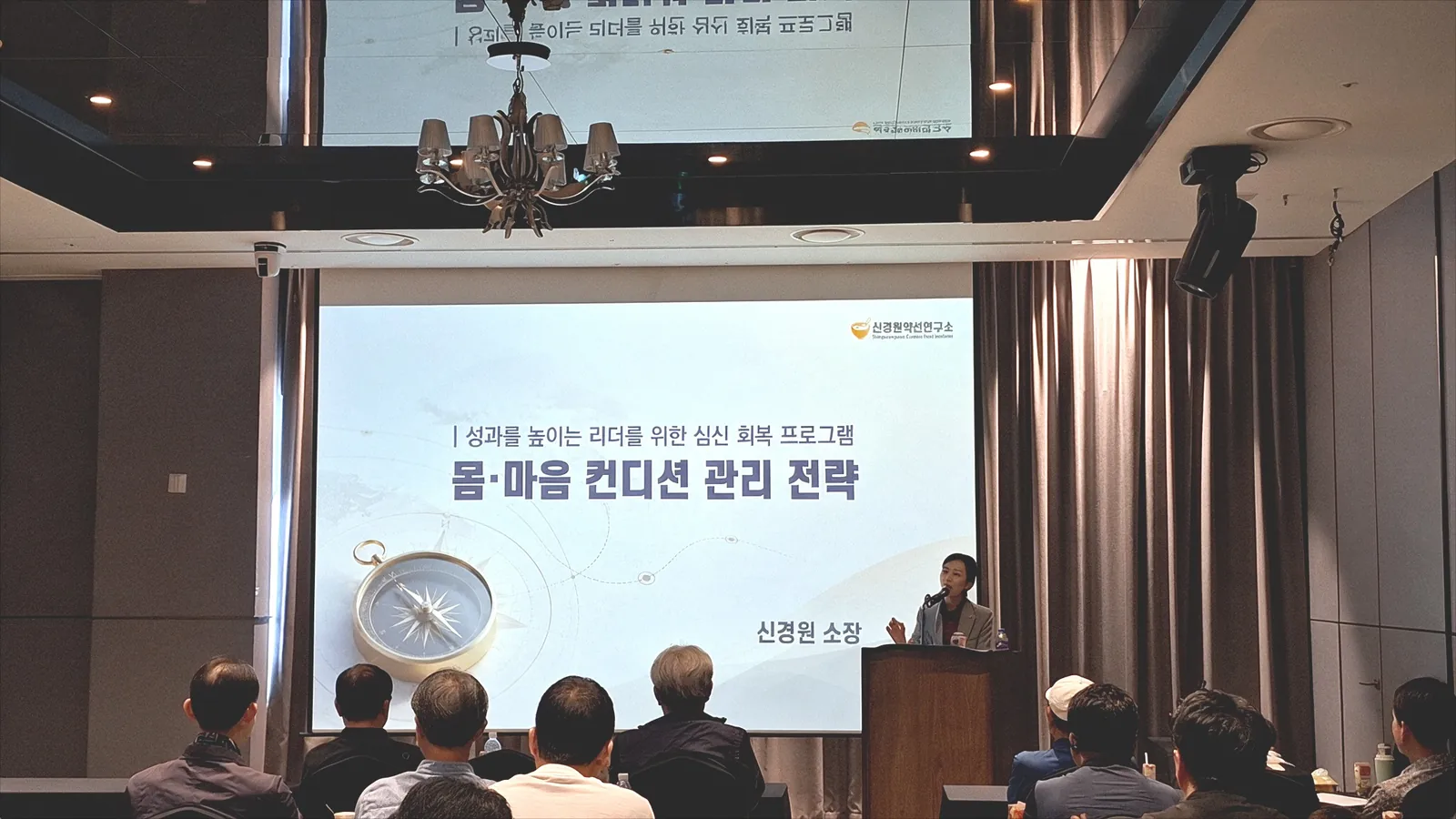 몸·마음 컨디션 관리 전략 슬라이드와 설명하는 강사, 강연에 집중한 참석 리더들의 뒷모습