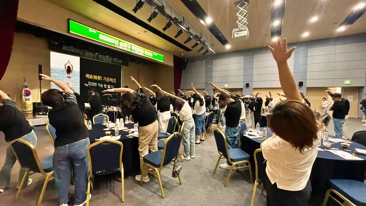 워크숍 참석자들이 서서 옆으로 몸을 기울이는 기공 스트레칭을 따라 하는 모습