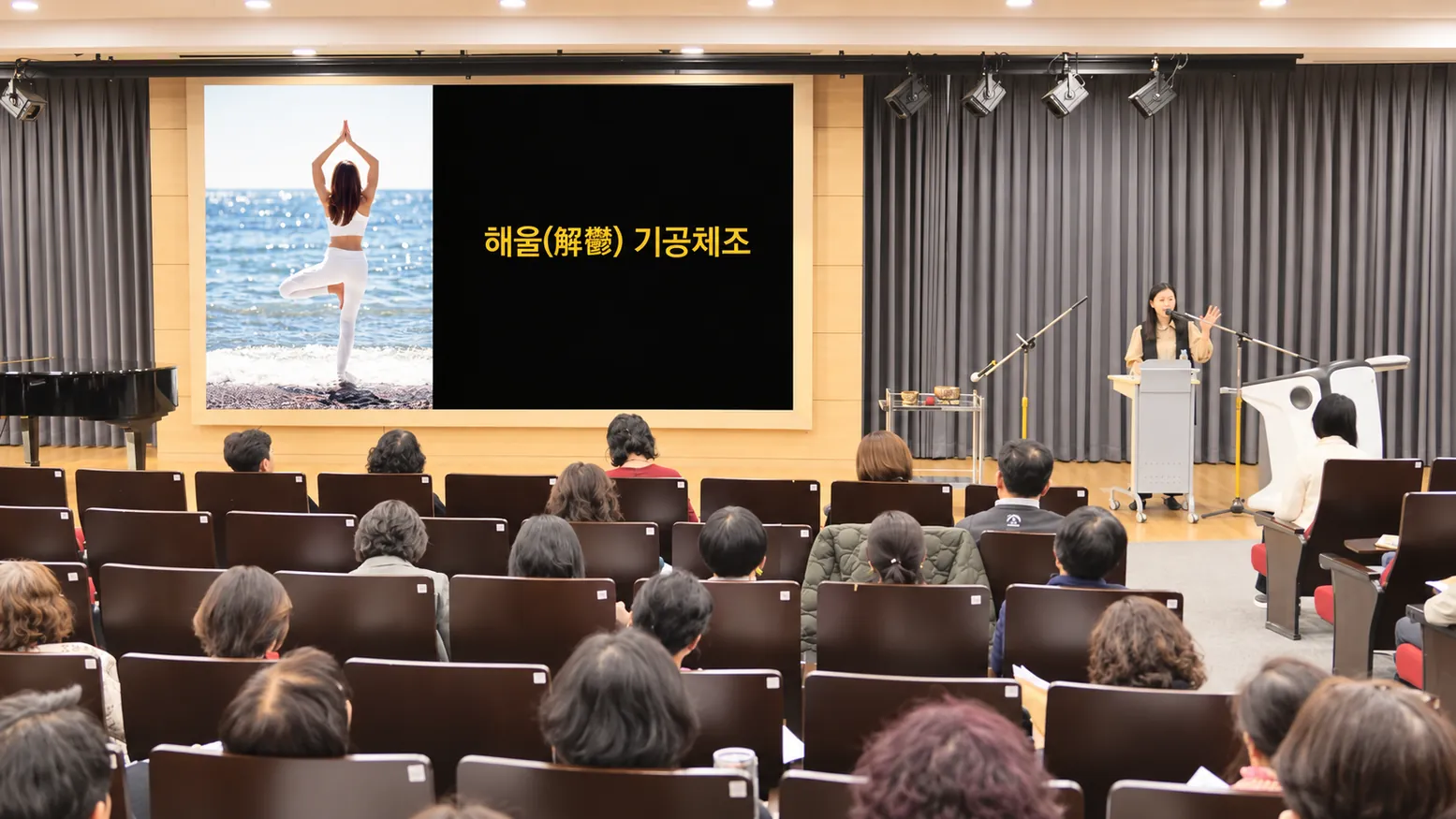 강사가 무대에서 양팔을 들어 기공체조 동작을 시범 보이는 모습